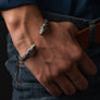 A close-up of a person's hand resting on their thigh, wearing two silver wolf-shaped cuff bracelets with intricate scrollwork.