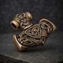 Angled side view of bronze Mjolnir pendant highlighting its carved Norse details and antiqued finish