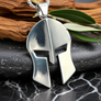 Silver Spartan helmet pendant on a dark surface with wooden and leaf background