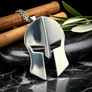 Silver Spartan helmet pendant on a dark surface with wooden sticks and leaves.