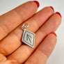 Silver Tiwaz pendant held between fingers with a plain background