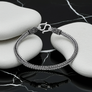 Silver braided bracelet on a reflective surface with a black background