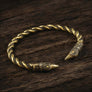 A twisted metal cuff bracelet with viking raven ends, shown on a dark wooden surface.