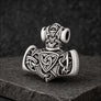 An antiqued silver Viking-style mace pendant with intricate Celtic knotwork and a triquetra symbol, displayed on a dark textured stone surface.