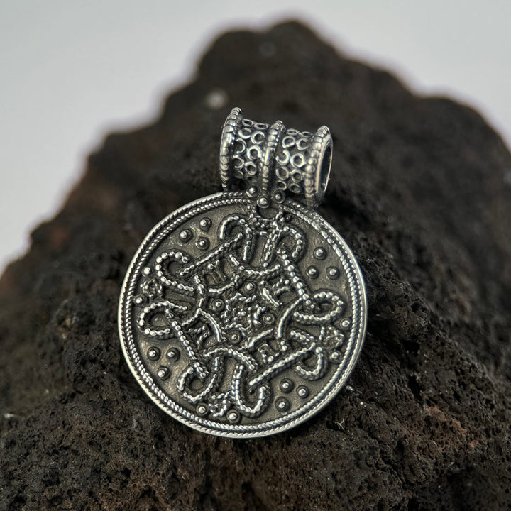 Silver Birka pendant with intricate design on a dark, textured surface