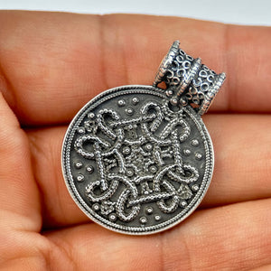 Silver Replica pendant with intricate design held in a hand