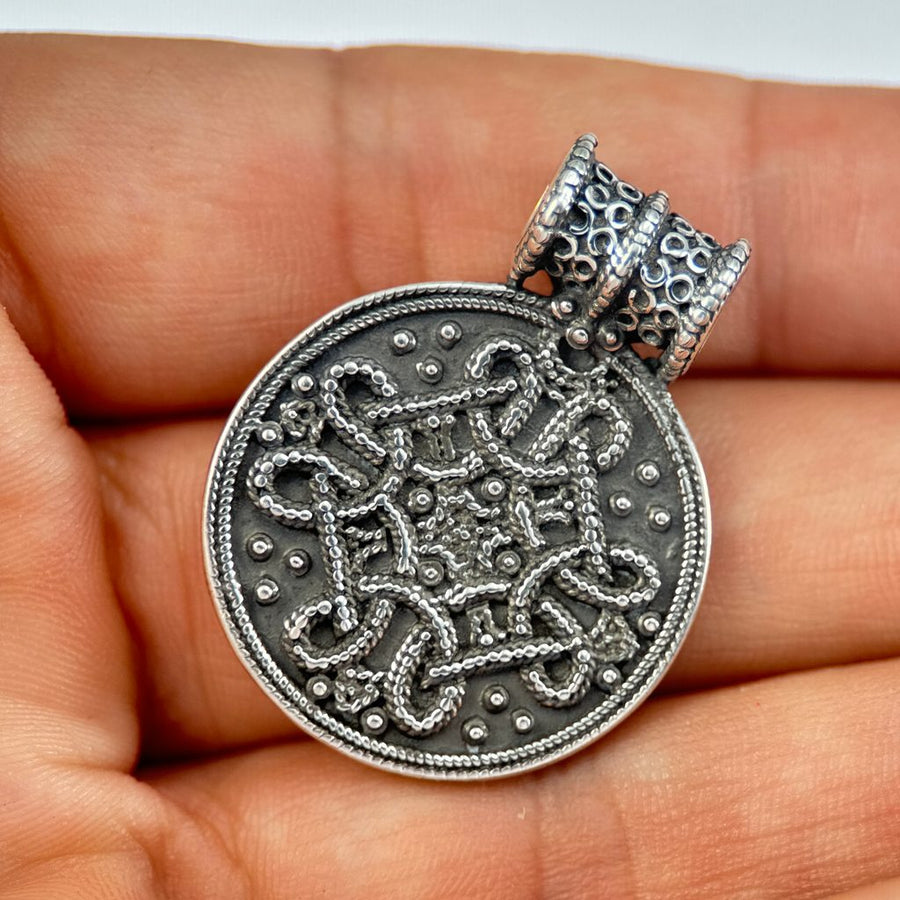 Silver Replica pendant with intricate design held in a hand