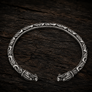 Open Viking dragon head armring in Italian silver-plated bronze with Norse-inspired detailing on dark rustic wood.