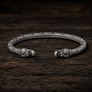 Open Viking dragon head armring in Italian silver-plated bronze with Norse-inspired detailing on dark rustic wood.