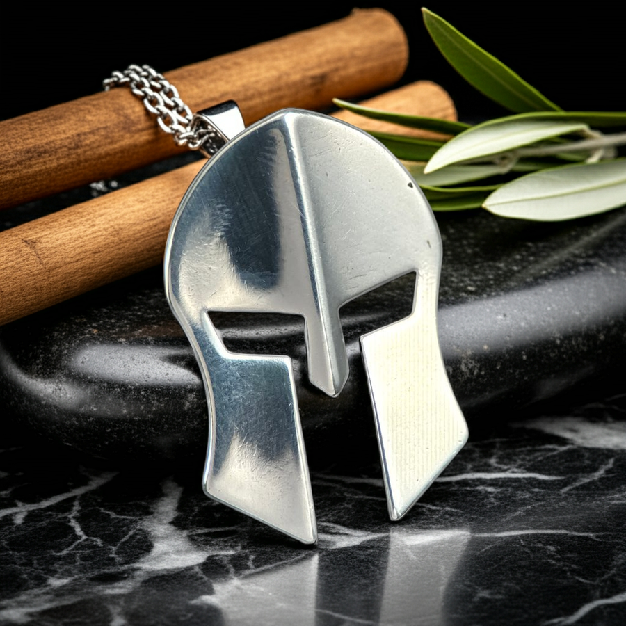 Silver Spartan helmet pendant on a dark surface with wooden sticks and leaves.