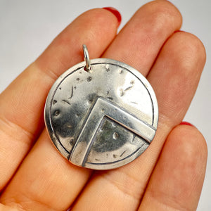 Silver Spartan shield pendant held in a hand with a plain background