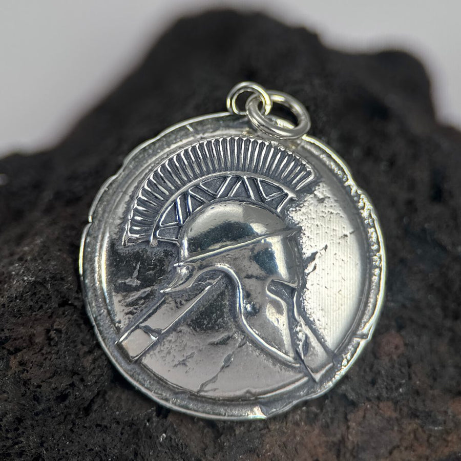 Silver Spartan helmet pendant on a dark stone surface