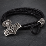 A black braided leather bracelet featuring a detailed silver-toned Viking hammer (Mjolnir) pendant and matching end caps, displayed on a dark slate background.