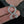Silver Troll Cross pendant held between fingers with a leafy background