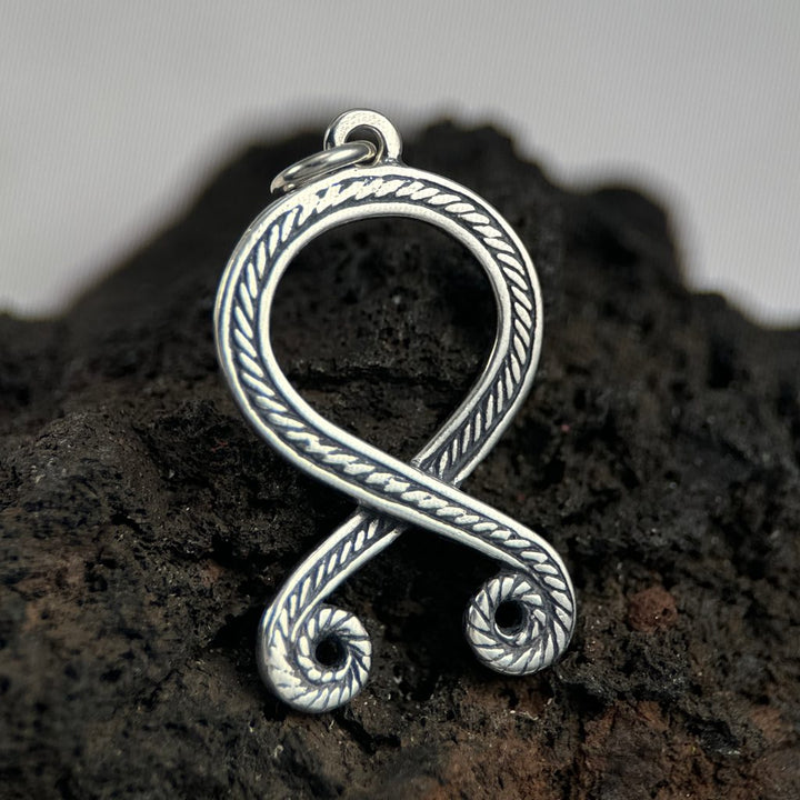 Silver Trolls cross pendant on a dark stone surface