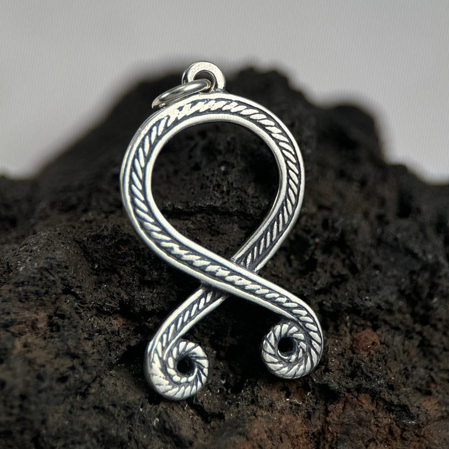 Silver Trolls cross pendant on a dark stone surface