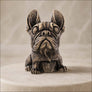 A small sculpted figurine of a French bulldog with a distressed metallic finish, sitting on a round beige pedestal against a soft beige background.