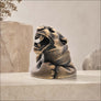 A roaring jaguar figurine with an open mouth and detailed mane, finished in a textured bronze and black finish, displayed on a light stone surface.