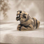 A sculpted stone jaguar statue in a roaring pose, positioned on a light stone ledge against a softly blurred beige background.
