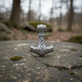 925 silver Thor’s hammer pendant with wolf head details on weathered stone with moss and blurred background