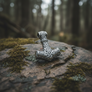 Geri and Freki wolf head Mjolnir pendant resting on a rock with forest bokeh background