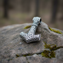 Silver Thor's hammer pendant on a stone surface with a blurred natural background