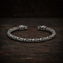 An oxidized sterling silver Viking-style cuff bracelet with intricate knotwork and wolf head closures, displayed on a dark rustic wooden surface.